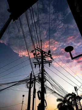 Dramatic sunset sky with silhouette of power lines and utility poles. Urban.. Stock Photos