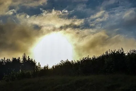 Dramatic sunset sky with sun peeking through clouds over dark forest silhouet Stock Photos