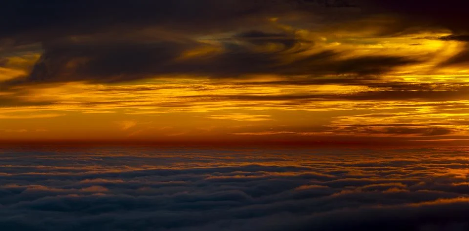 Dramatic sunset sky with vibrant orange and dark clouds over a sea of clouds Stock Photos