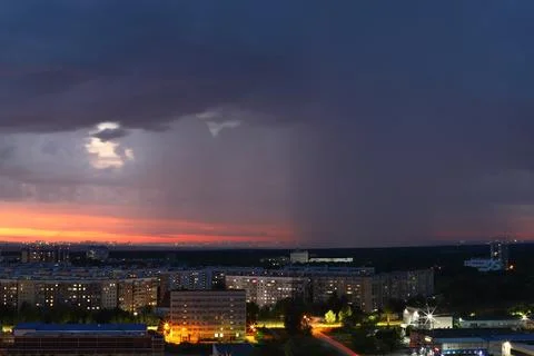 A dramatic sunset with storm clouds and rain over the cityscape Stock Photos