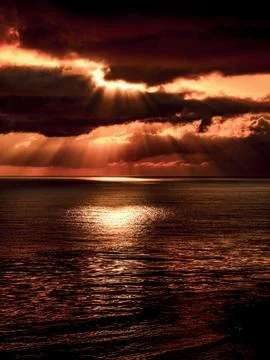 Dramatic sunset with sunbeams breaking through dark clouds over the ocean c.. Stock Photos