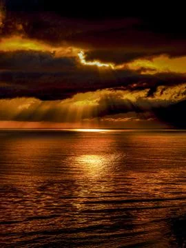 Dramatic sunset with sunbeams breaking through dark clouds over the ocean Stock Photos