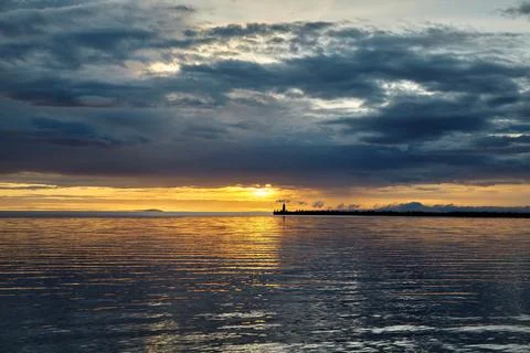 Dramatic sunset with thunderclouds before the storm. Sea pier with a lighthouse Stock Photos