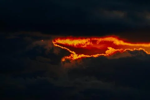 Dramatic sunset with vibrant orange and red hues peeking through dark storm.. Stock Photos