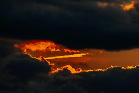 Dramatic sunset with vibrant orange and red hues peeking through dark storm.. Stock Photos