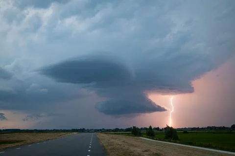 Dramatic supercell thunderstorm with lightning strike and wall cloud at dusk. Stock Photos