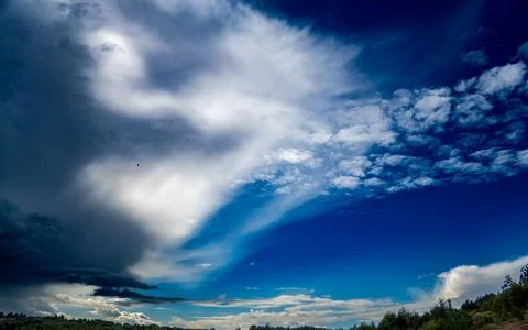 Dramatic Swirling Clouds Over Deep Blue Sky and Forest Horizon Stock Photos