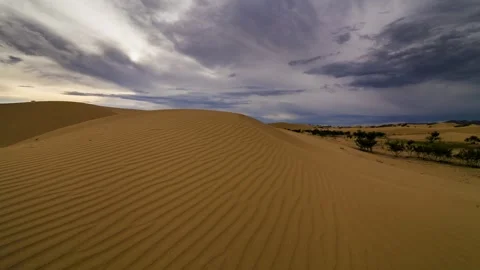 Dramatic thunderstorm clouds gathering over golden sand dunes in a remote desert 스톡 동영상 347040529