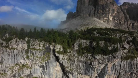 Dramatic vertical cliff with pine trees, sweeping Dolomites panorama; hiker Stock Footage 325753933