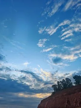 Dramatic vertical cloudscape over a silhouetted red earth hill at dusk Фото