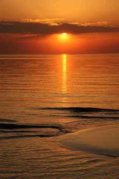 Dramatic vertical sunset over the sea coast. The sun hides behind dark clouds Stock Photos