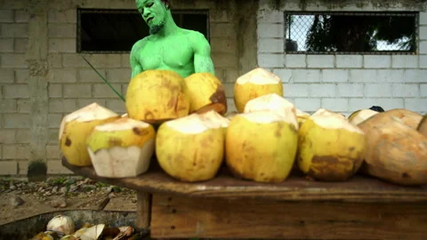 Dramatic video of painted green man sellin* coconuts in small Caribbean coastal  Stock Footage 142467160