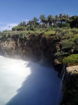 Dramatic view of a cliffside waterfall dropping into misty white sea waves. Stock-Fotos