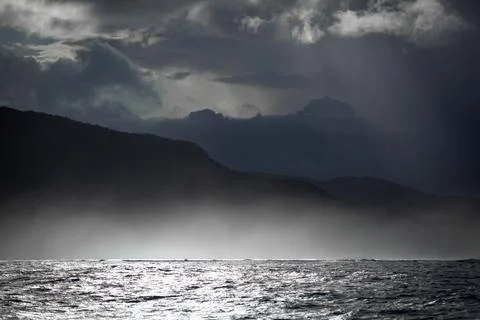 Dramatic View of the Sea Beneath Ominous Storm Clouds and Mountain Silhouette Фото