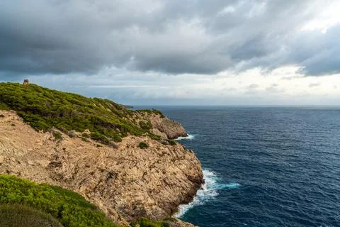 Dramatic view of waves crashing against rocky shoreline under gray storm clou Stock Photos
