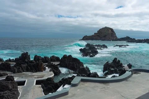 Dramatic Volcanic Coastline with Crashing Waves and Distant Island Under Cl.. Stock Photos