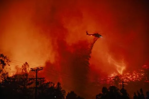 Dramatic water dropping helicopter over a brush fire at night Stock Photos