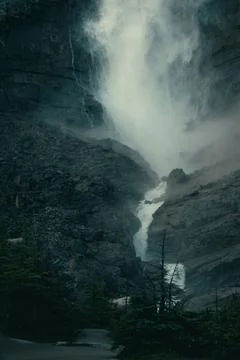Dramatic waterfall cascading down rocky mountain face into the misty abyss. Stock Photos