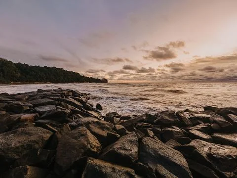 A dramatic wide-angle shot of a rocky breakwater at sunset beach Stock Photos