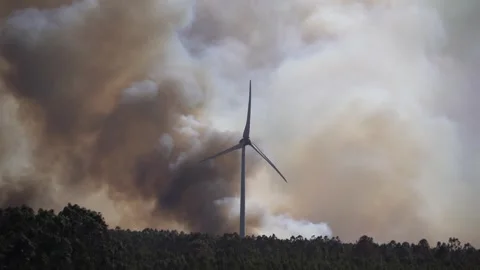 A dramatic wildfire burns near a windmill under a sky filled with thick clouds Stock Footage 317525749