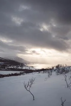 Dramatic winter light breaks through dark clouds over Malangen fjord near T.. Stock Photos