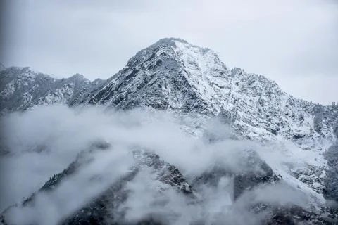 A dramatic winter scene of a snow-covered mountain peak emerging from swirlin Stock Photos