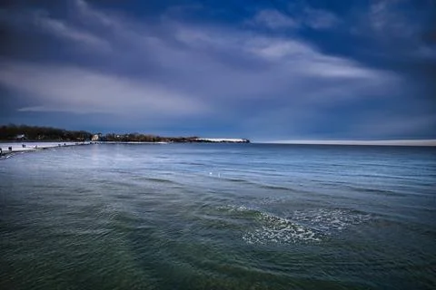 A dramatic winter seascape shows a wide, calm ocean with gentle waves rolli.. Stock Photos