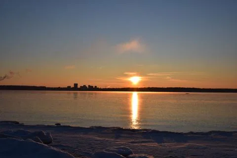 Dramatic Winter Sunset Over Frozen Bay with Distant City Horizon Stock Photos
