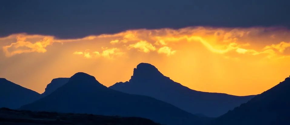 Dramatic yellow orange sunset over mountains with storm clouds, Lesotho Stock Photos