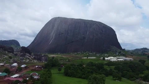 Dramatic Zuma Rock landscape contrasted with rural housing, featuring lush Stock Footage 314403662