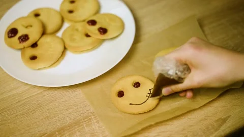 Drawing a funny chocolate face on a plain baked cookie close up Stock Footage 342704189