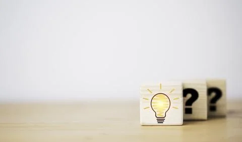 Drawing glowing lightbulb in front of question mark which print on wooden c.. 스톡 사진