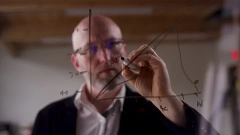 Drawing graphs on clear plexiglass with a dry erase marker by a businessman Stock-Footage 133285099