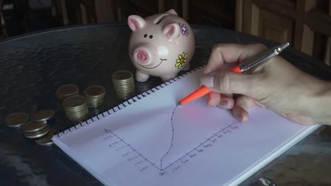 Drawing a growing graph and putting a euro coin into a pig thrift-box Stock Footage 82361376