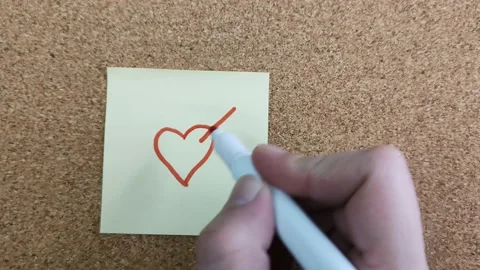 Drawing a HEART with a red felt-tip pen on a yellow paper sticker Stockbeeldmateriaal 170087581