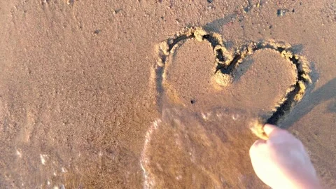 Drawing a heart to sand and waves wash it away Stock Footage 157545367