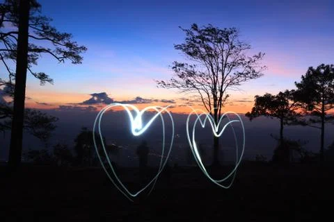Drawing light two hearts by flashlight in the air in the forest before sunris Stock Photos