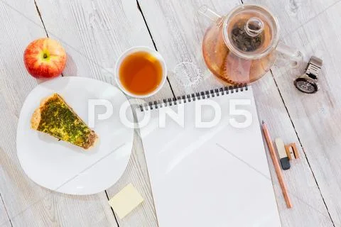Drawing-pad, cup of tea, chicken pie, apple, glass teapot and watch on wooden Stock Photos