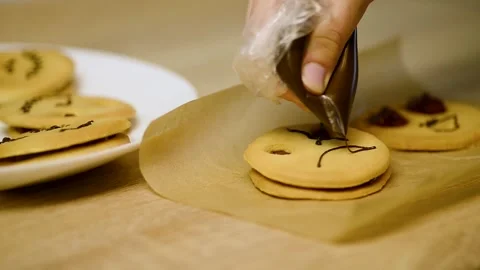 Drawing a pirate face on a baked cookie using a chocolate pastry bag Stock Footage 342704237