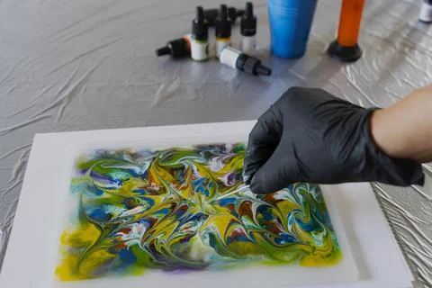 Drawing process with alcohol ink on liquid. A female hand in a glove with a w Stock Photos