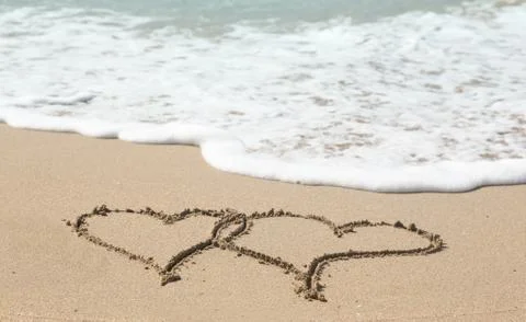 Drawing in sand by ocean of two hearts Stock Photos