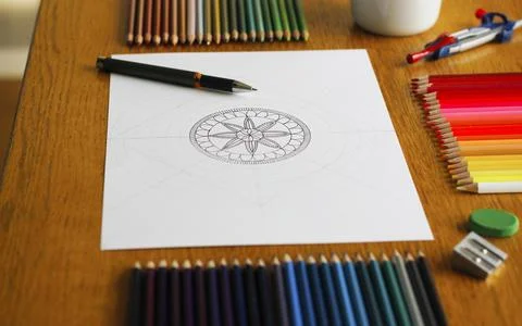 A drawn mandala pattern on white paper lying on a wooden table Stock Photos