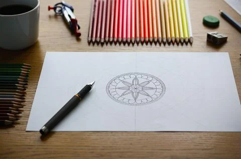 A drawn mandala pattern on white paper lying on a wooden table Stock Photos