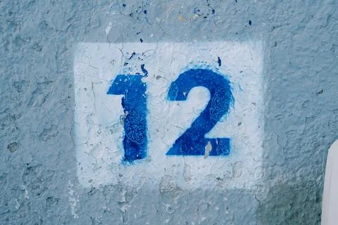 Drawn number twelve in a white rectangle on a blue peeling wall Stock Photos