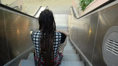 Dreadlock person sitting on moving escalator Stock Footage 25734065