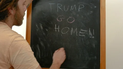 A dreadlocks man write Trump go home on a blackboard Stock-Footage 86473217