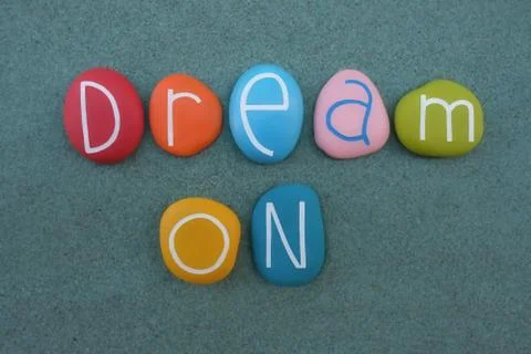 Dream on, creative text composed with multicolored stone letters over green sand Stock Photos
