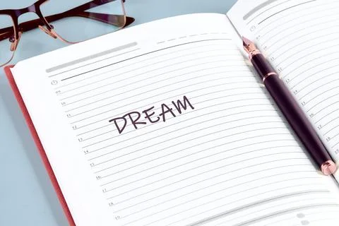 DREAM on an open planners white page, with pen  glasses on a blue desk, ready Stock Photos