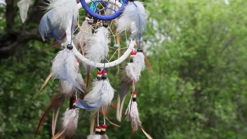 A dreamcatcher with multi-colored feathers flutters in the wind against the Stock Footage 151203499