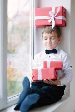 Dreaming boy sitting by the window with a gift box on head 스톡 사진